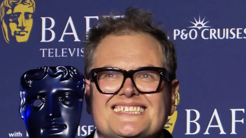 Celebrity Traitors winner Alan Carr smiling in glasses and a tuxedo, holding a BAFTA mask trophy