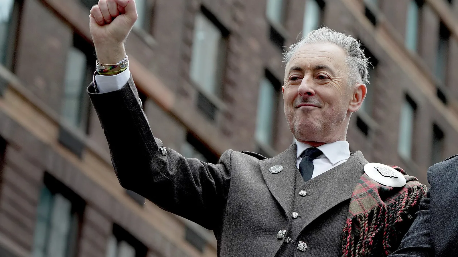 The Traitors US host Alan Cumming in a tweed kilt jacket, raising a fist and smiling in New York