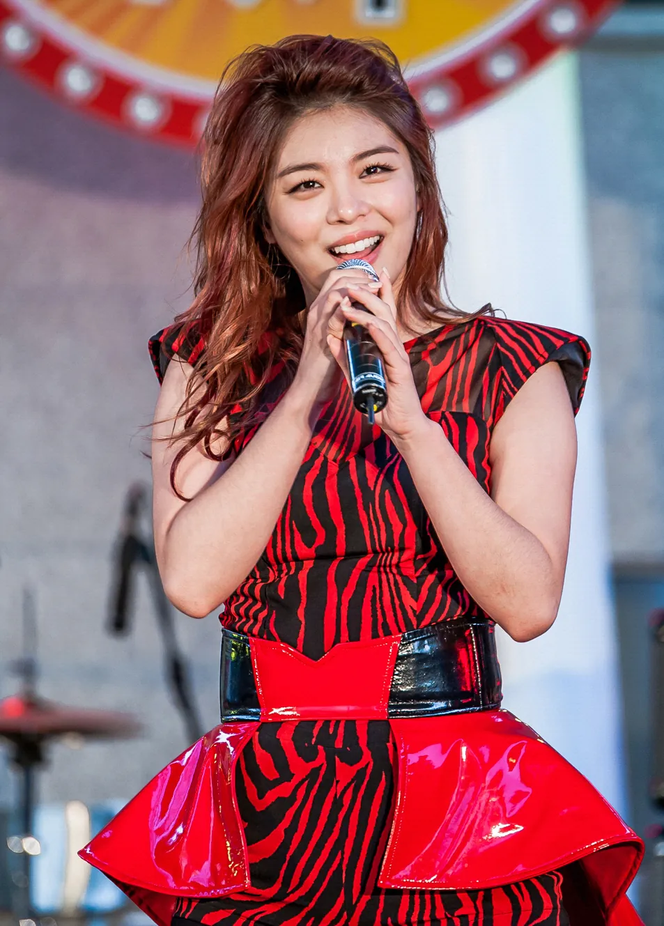 Singer Ailee in a red and black dress singing into a microphone on an outdoor stage