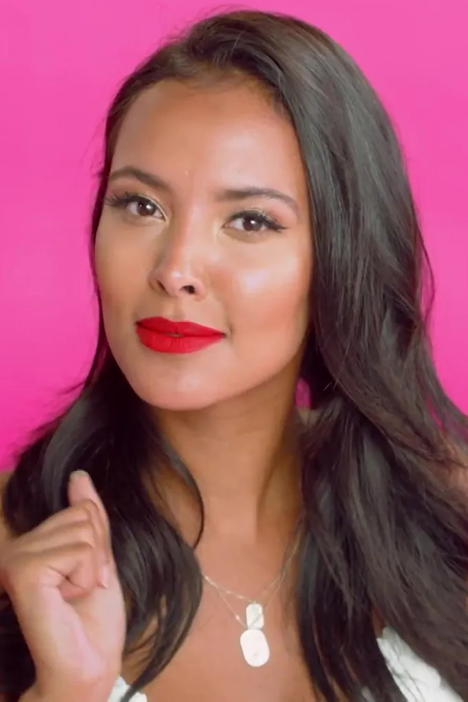 Maya Jama with long dark hair and red lipstick in front of a pink backdrop