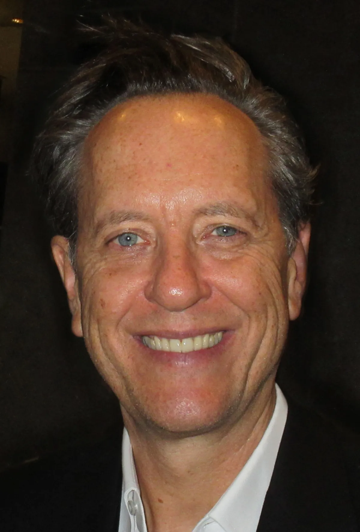 Richard E. Grant smiling in a dark jacket